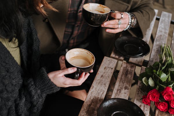 Faceless couple with cups of coffee and roses in cafeteria